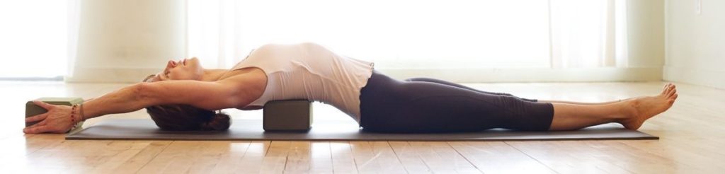 Bo lying over a block, face up, with her legs stretched out arms overhead and another block between her hands
