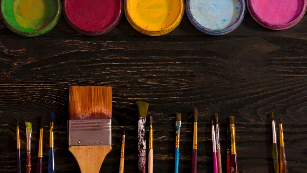 several paint colors laid out over a dark brown background with paintbrushes opposite them